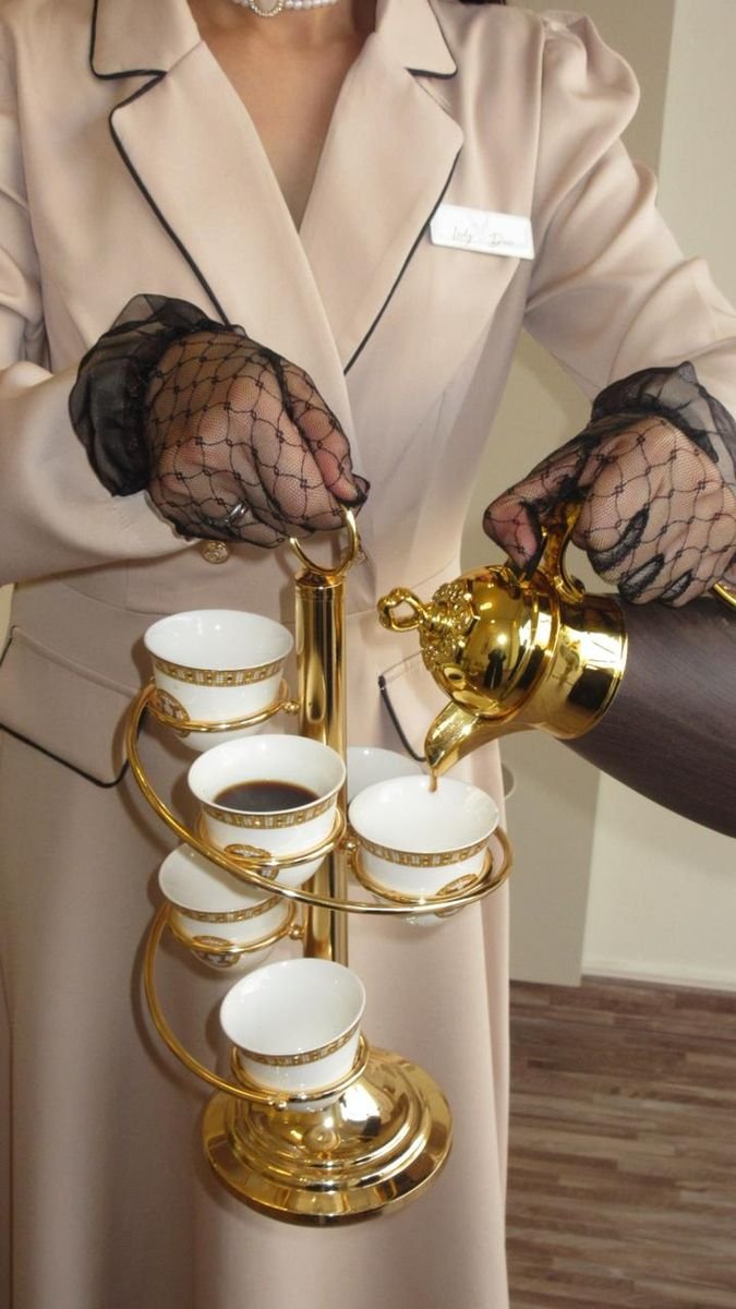 Lady Deer hostess pouring Arabic coffee from a gilded dallah